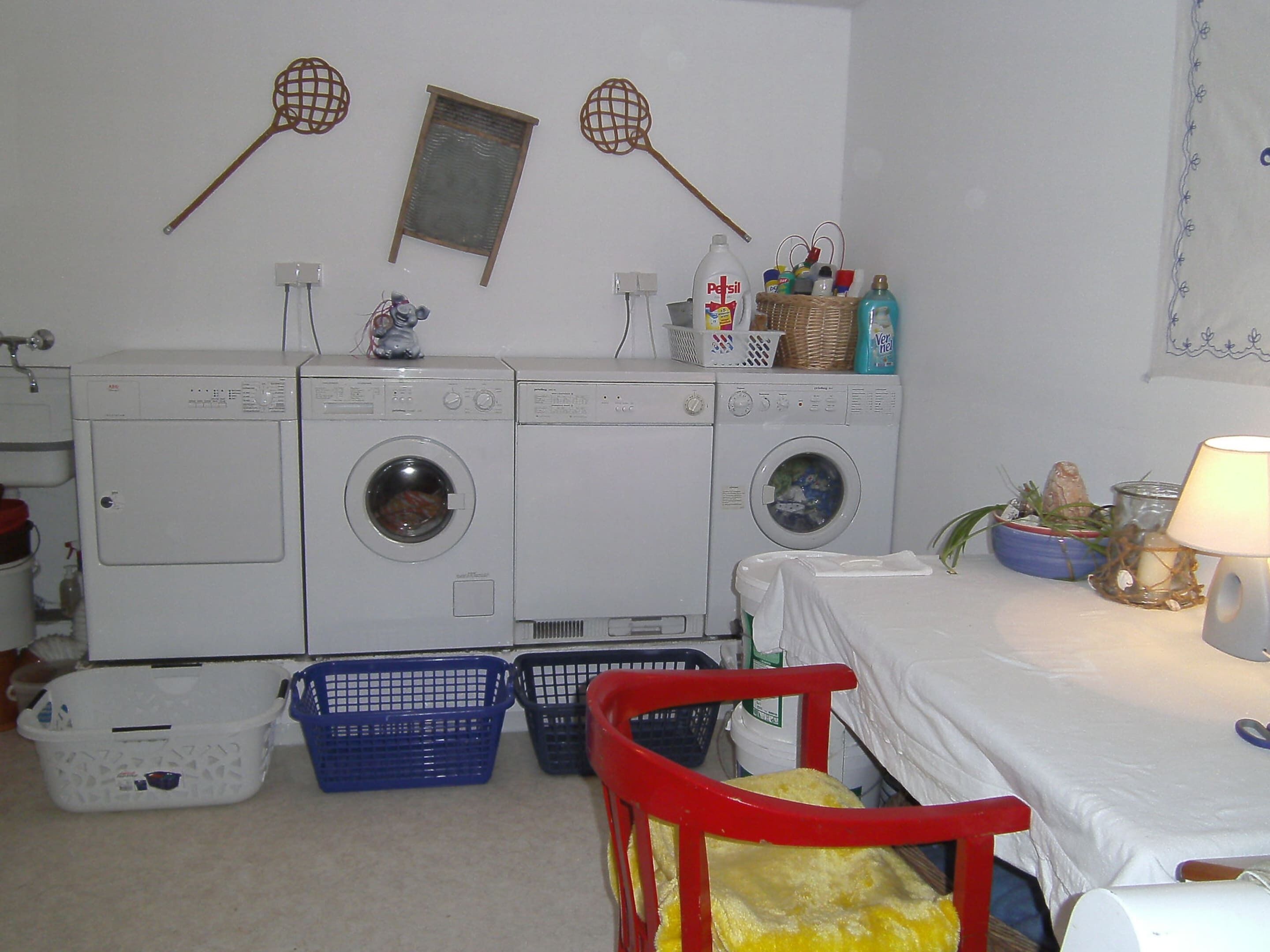 A laundry room with two front-loading washing machines, a red chair, and a bed with a white sheet.