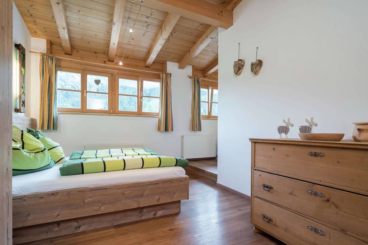 Ein Schlafzimmer mit einem Holzbett, einem Schminktisch und zwei mit Vorhängen versehenen Fenstern.