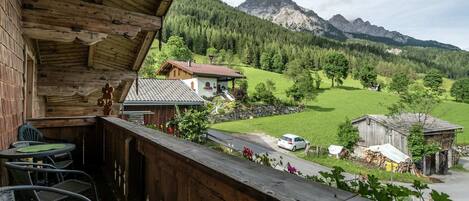 Un balcón de madera con vistas a un paisaje montañoso, que incluye casas y un coche aparcado en la carretera.