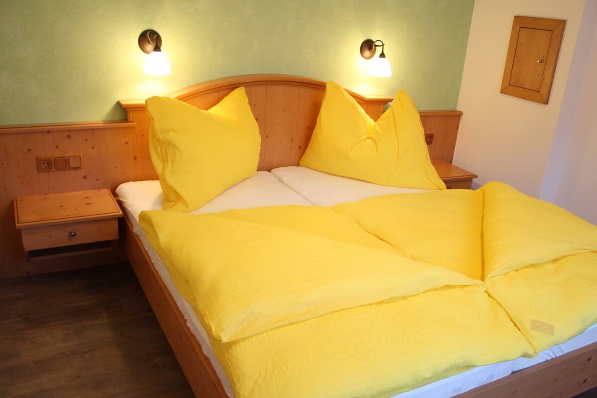 Ein Bett mit Holz Kopfteil, zwei Nachttische und ein Beistelltisch mit Schublade.