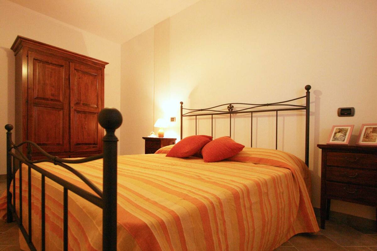 A bedroom with a bed, wooden wardrobe, bedside table, lamp, and a small dresser.