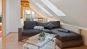 Un dormitori tipus loft modern amb sostre inclinat, una taula de cafè de vidre i un sofà modular gris.