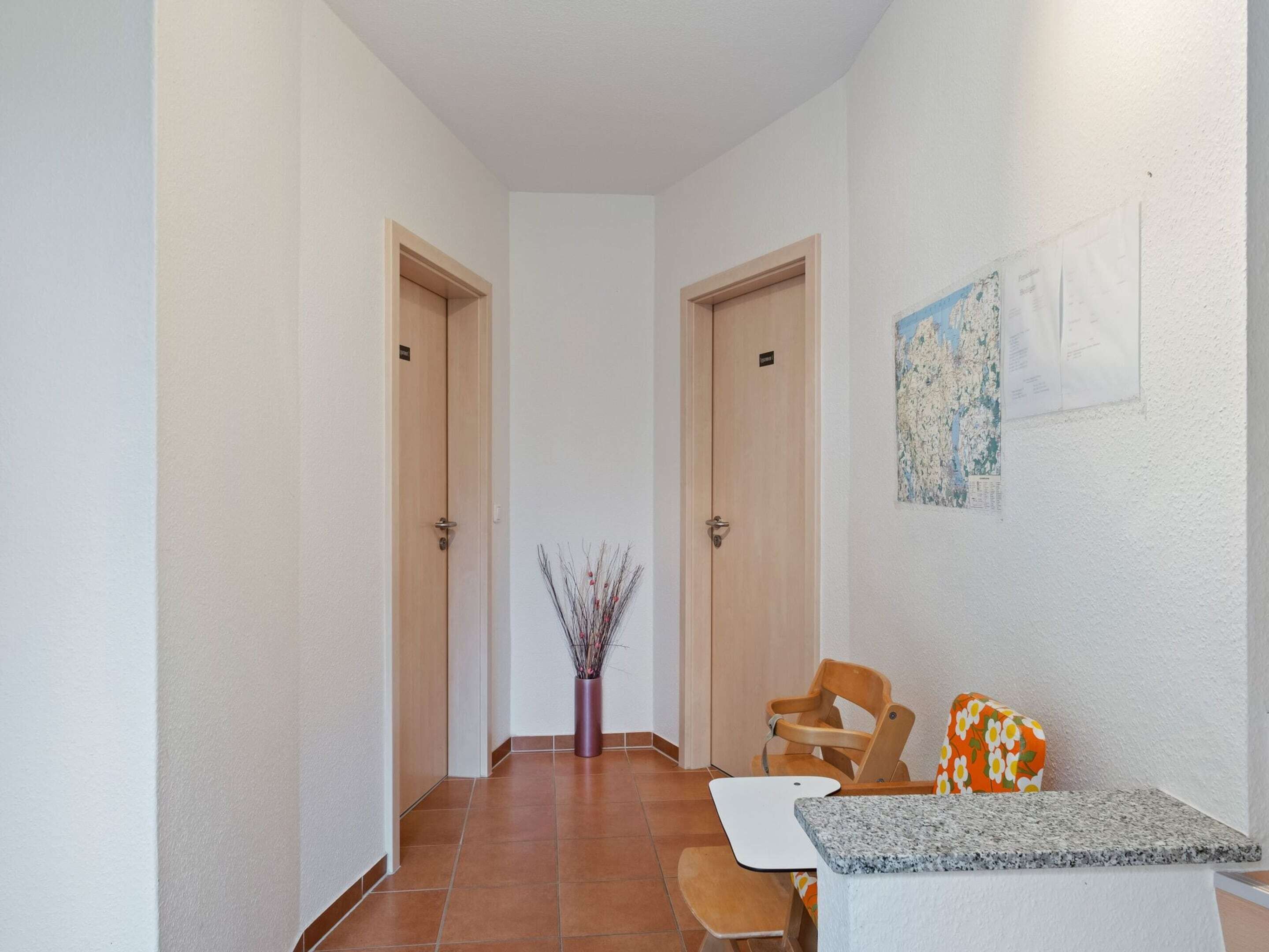 A hallway with two doors, a vase with branches, a small table with a white top, and a chair with an orange floral cushion.