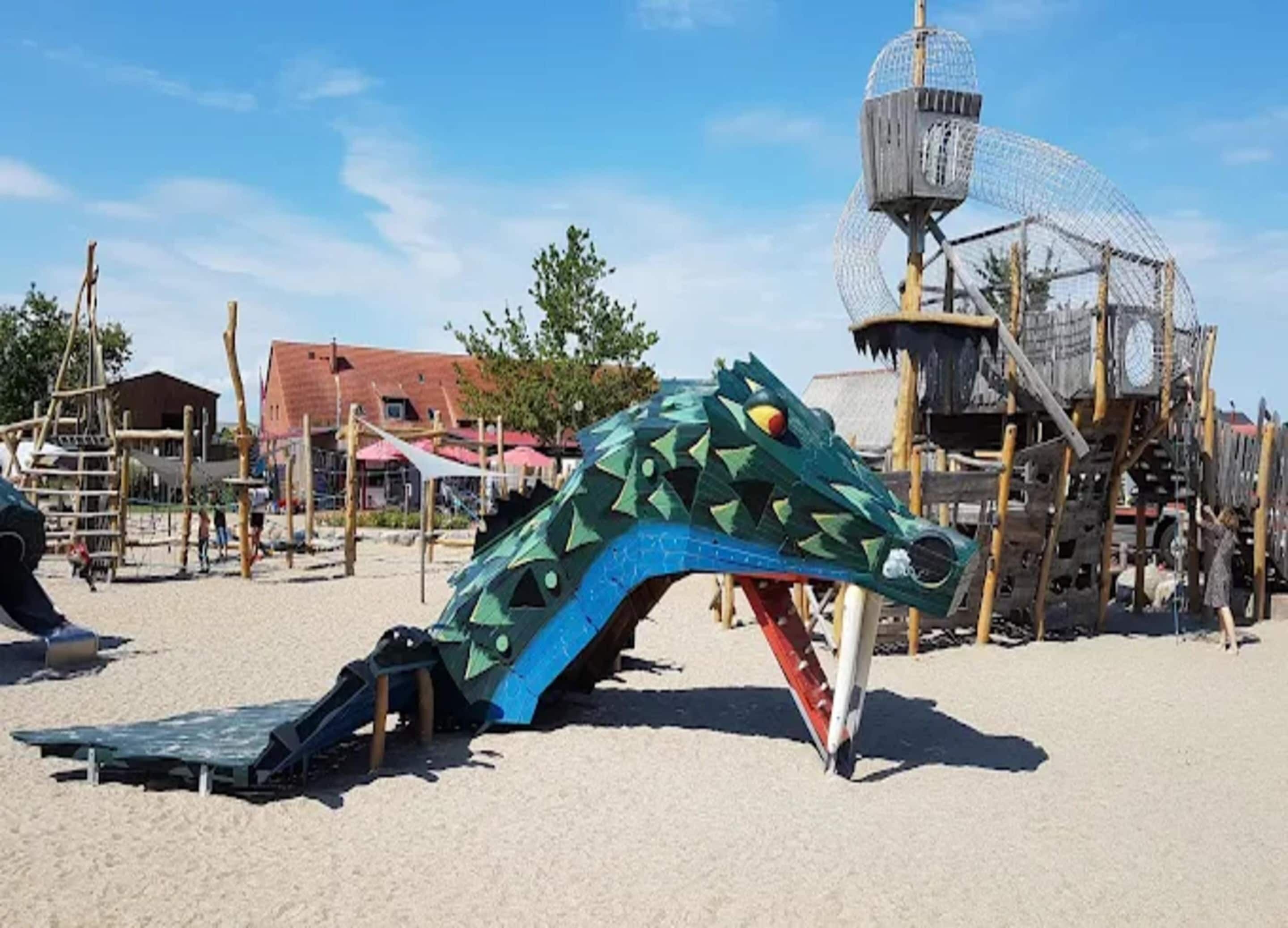Een speelplaats met een grote speelconstructie in de vorm van een draak, een klimnet en een glijbaan.