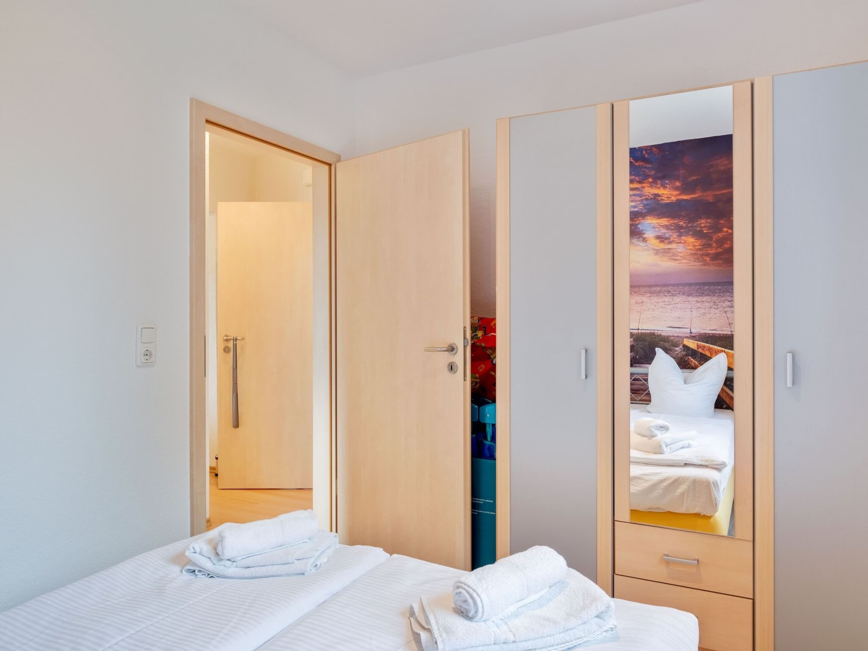 A hotel room with a bed, a wardrobe with a mirror, and a view of the beach through the mirror.