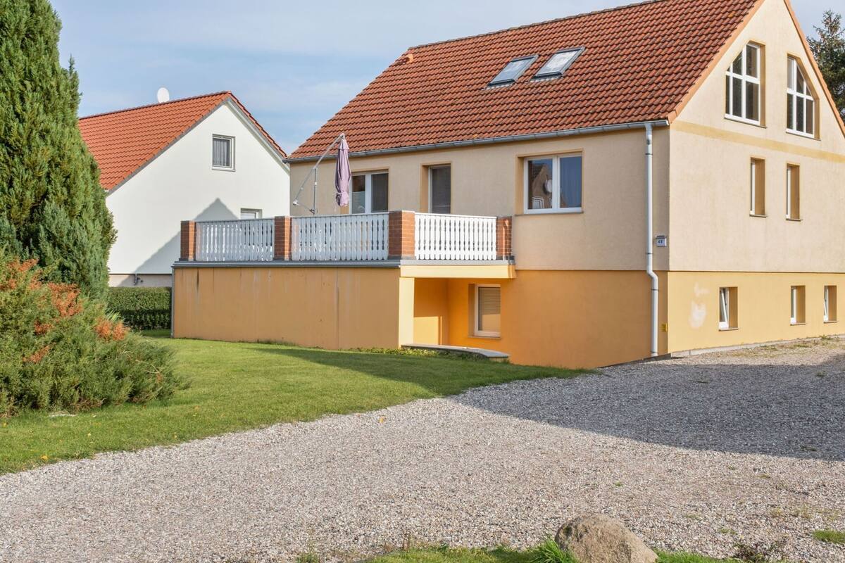 Ein zweigeschossiges Wohnhaus mit rotem Ziegeldach, einem Balkon mit weißer Geländer und einer Auffahrt mit Kiesbefestigung.