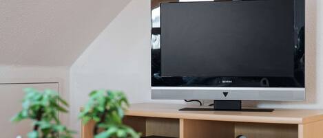 Una sala de estar moderna con un televisor de pantalla plana sobre un mueble de madera, una mesa de centro de vidrio y dos plantas en macetas.