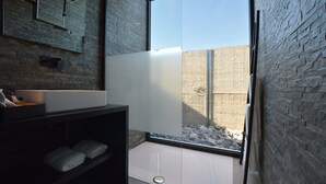 Een moderne badkamer met een grote spiegel, een wit wastafeltje en een raam met uitzicht op een rotsachtig gebied.