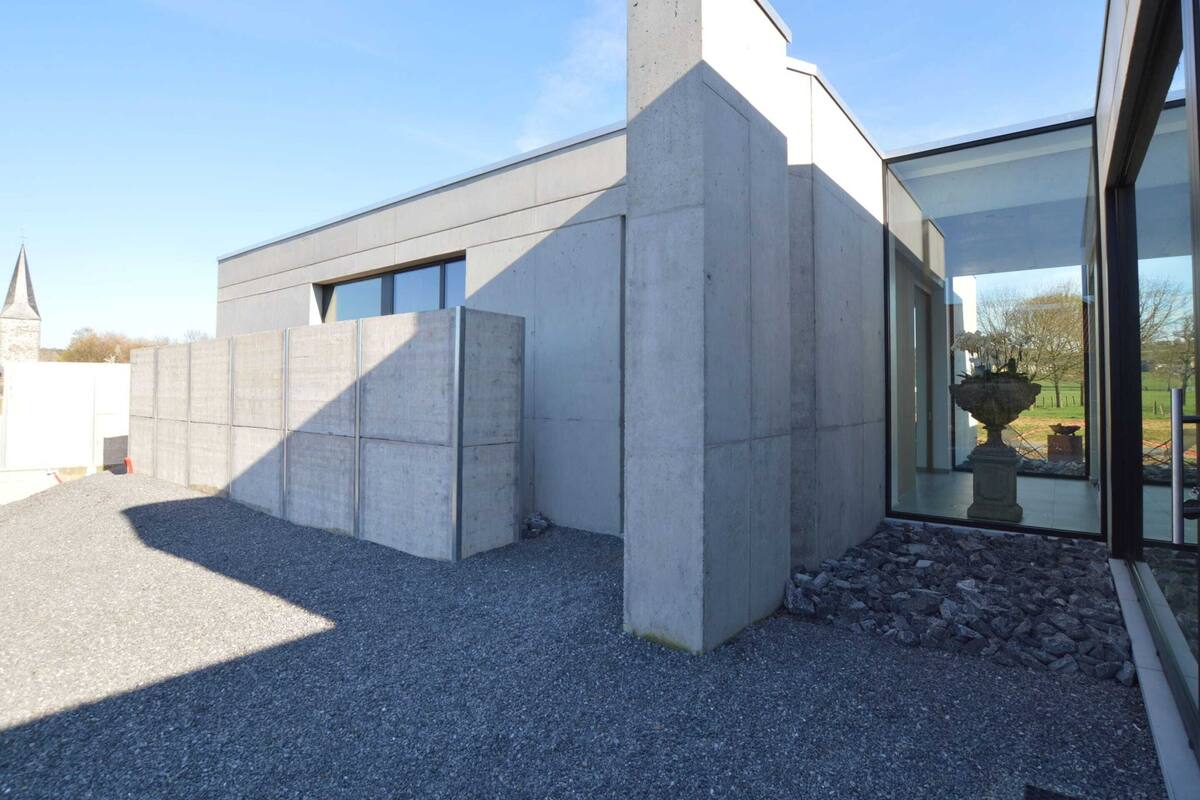 Ein modernes Gebäude mit einer Betonfassade, großen Fenstern und einer Schotterauffahrt.