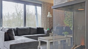 Ein modernes Wohnzimmer mit einer Eckcouch, einem Kamin aus Glas und Blick auf Bäume.