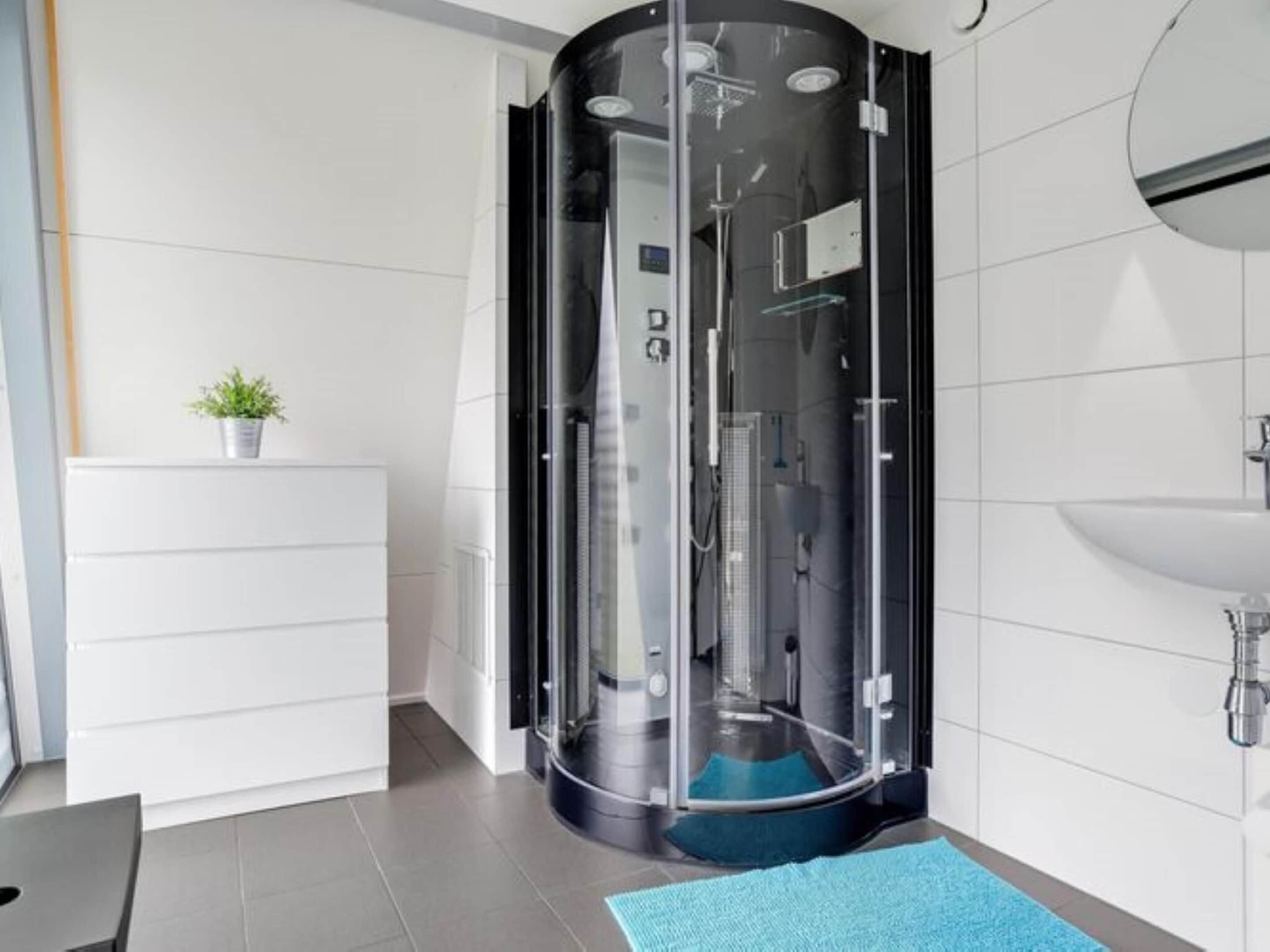 Une salle de bain moderne avec une douche à parois de verre, un lavabo blanc et une petite plante en pot posée sur un meuble blanc.