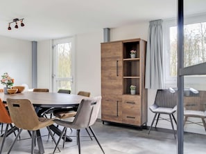 A modern dining area with a wooden table and chairs, a tall cabinet with shelves, and large windows with curtains.