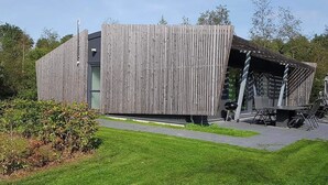 Ein modernes Gebäude mit Holzfassade, einer überdachten Außenbestuhlung und einem gepflegten Rasen.