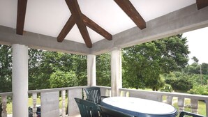A covered outdoor patio with a round table and chairs, surrounded by white columns and a view of greenery.