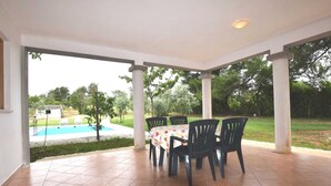 A covered patio with a pool view, outdoor seating, and a tiled floor.