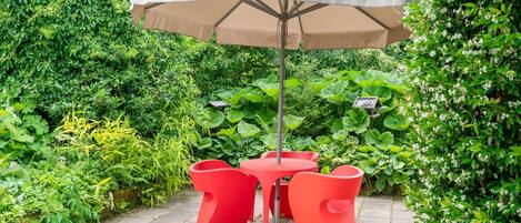 A patio with a table and chairs, surrounded by lush greenery.