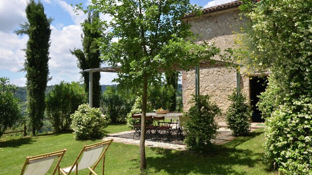 Un jardin agrémenté d’une pergola, d’une table avec des chaises et d’un bâtiment en pierre.