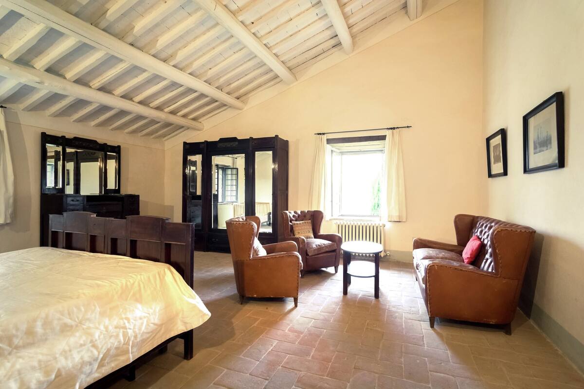 A spacious room with a large bed, two armchairs, a small table, and a desk.