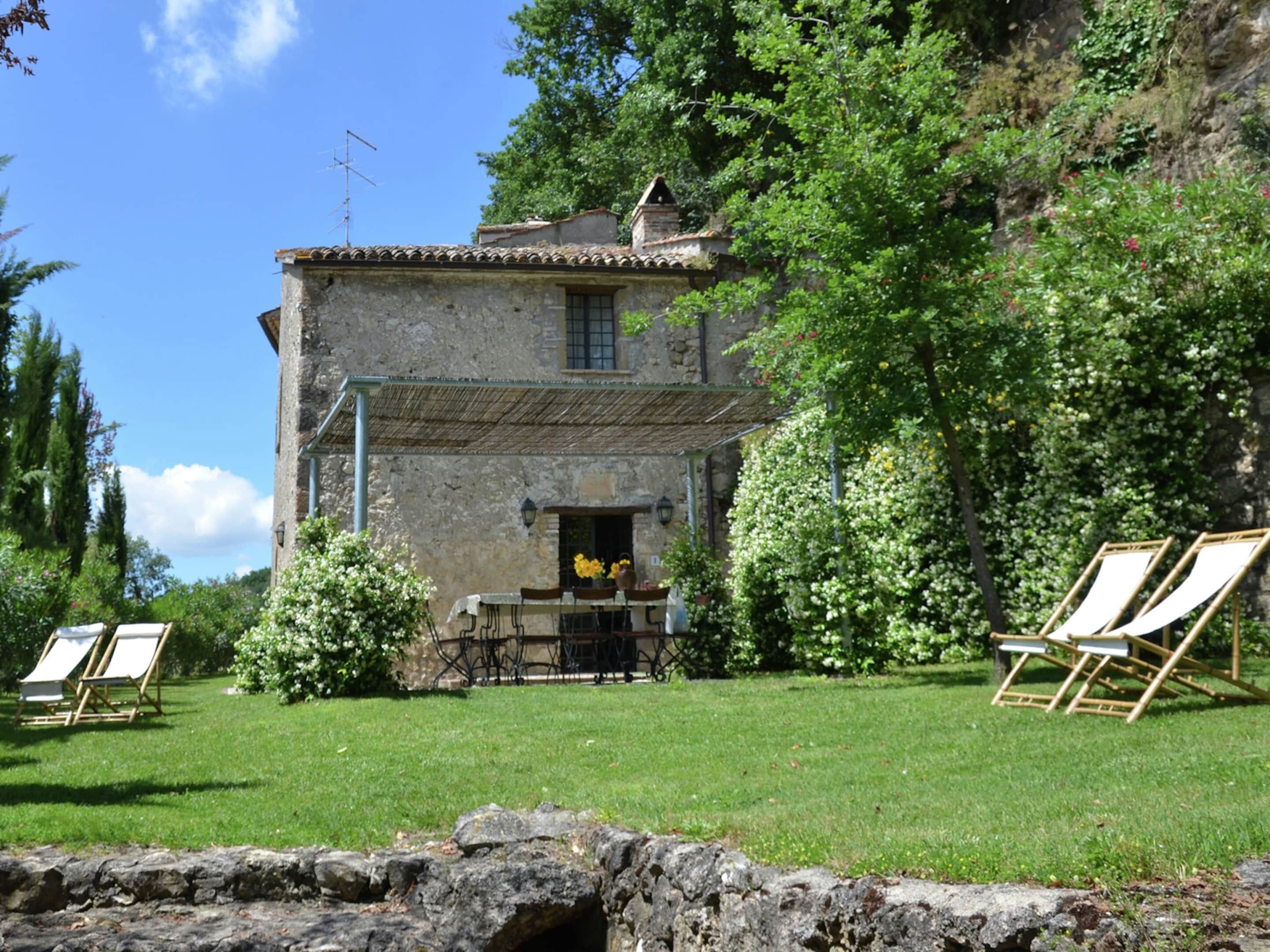 A stone building with a rustic exterior, a small patio with a table and chairs, and a grassy lawn.
