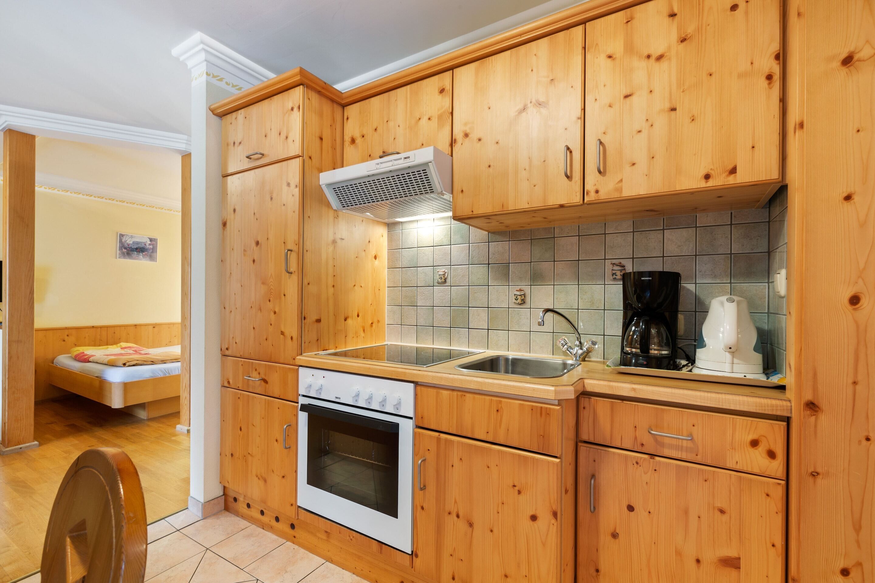 A compact kitchen with wooden cabinets, a built-in oven, a sink, and a coffee maker.