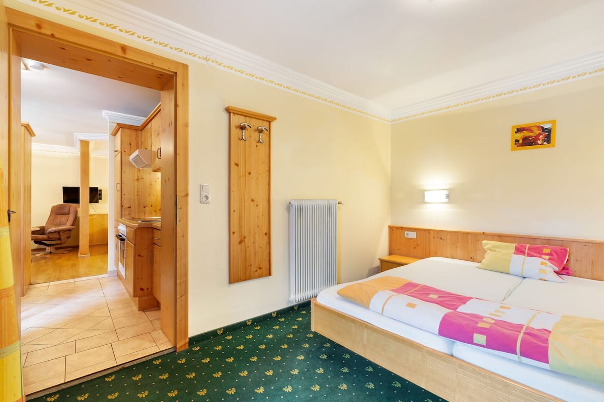 A hotel room with a bed, a wooden wardrobe, a radiator, and a door leading to a bathroom.
