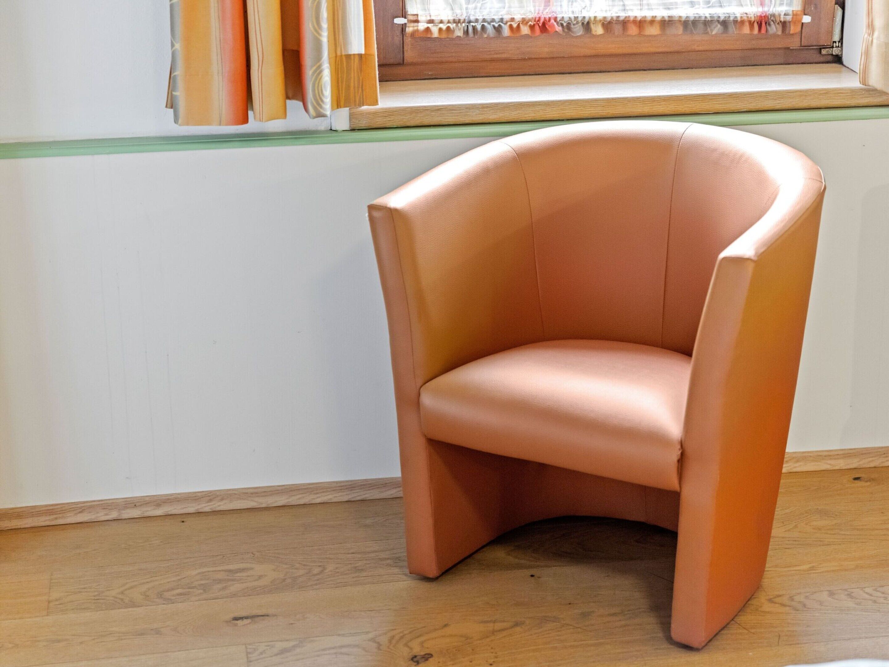 A corner chair in a room with wooden flooring and a window with curtains.