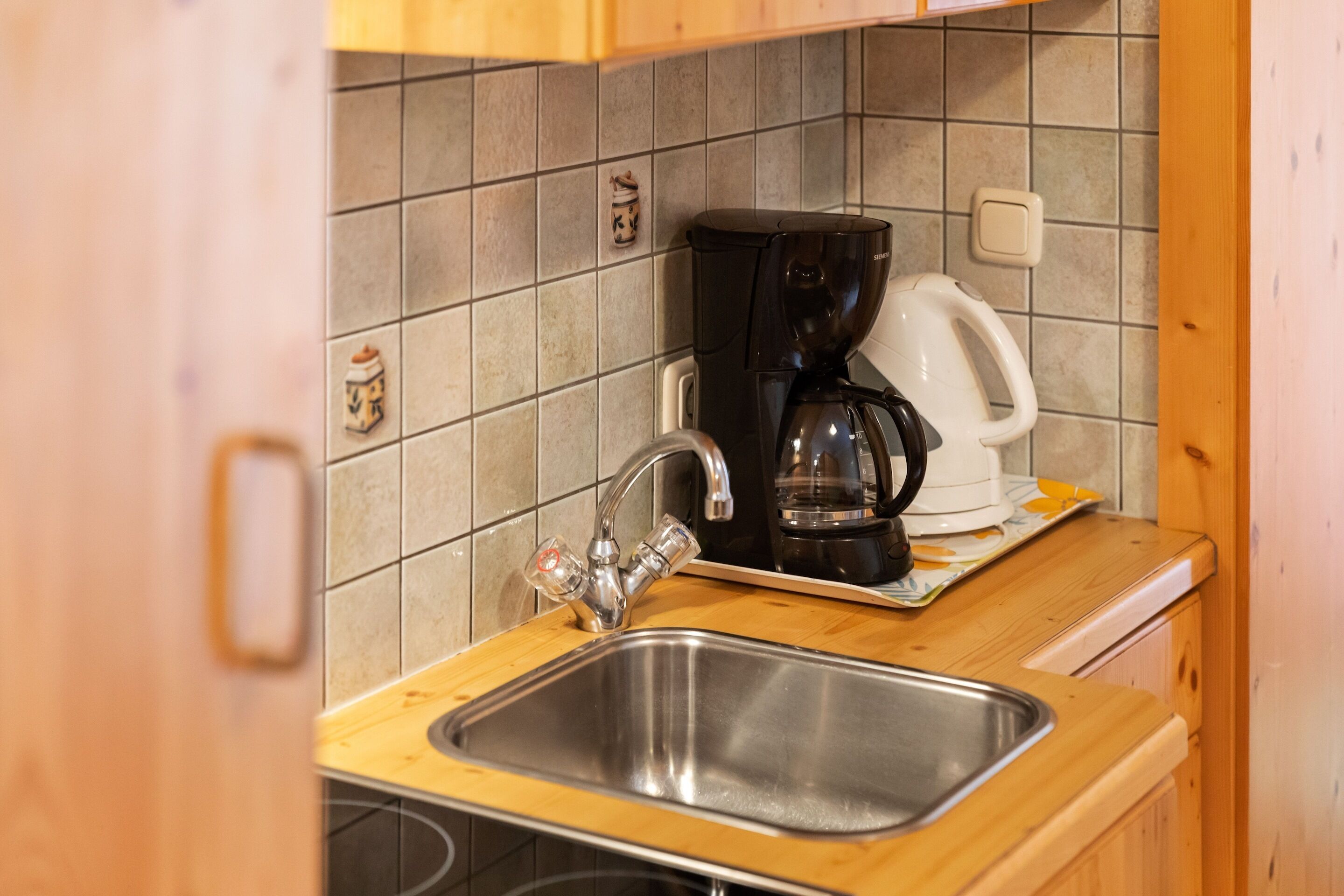 A kitchen with a stainless steel sink, a black coffee maker, and a white coffee pot on a wooden countertop.