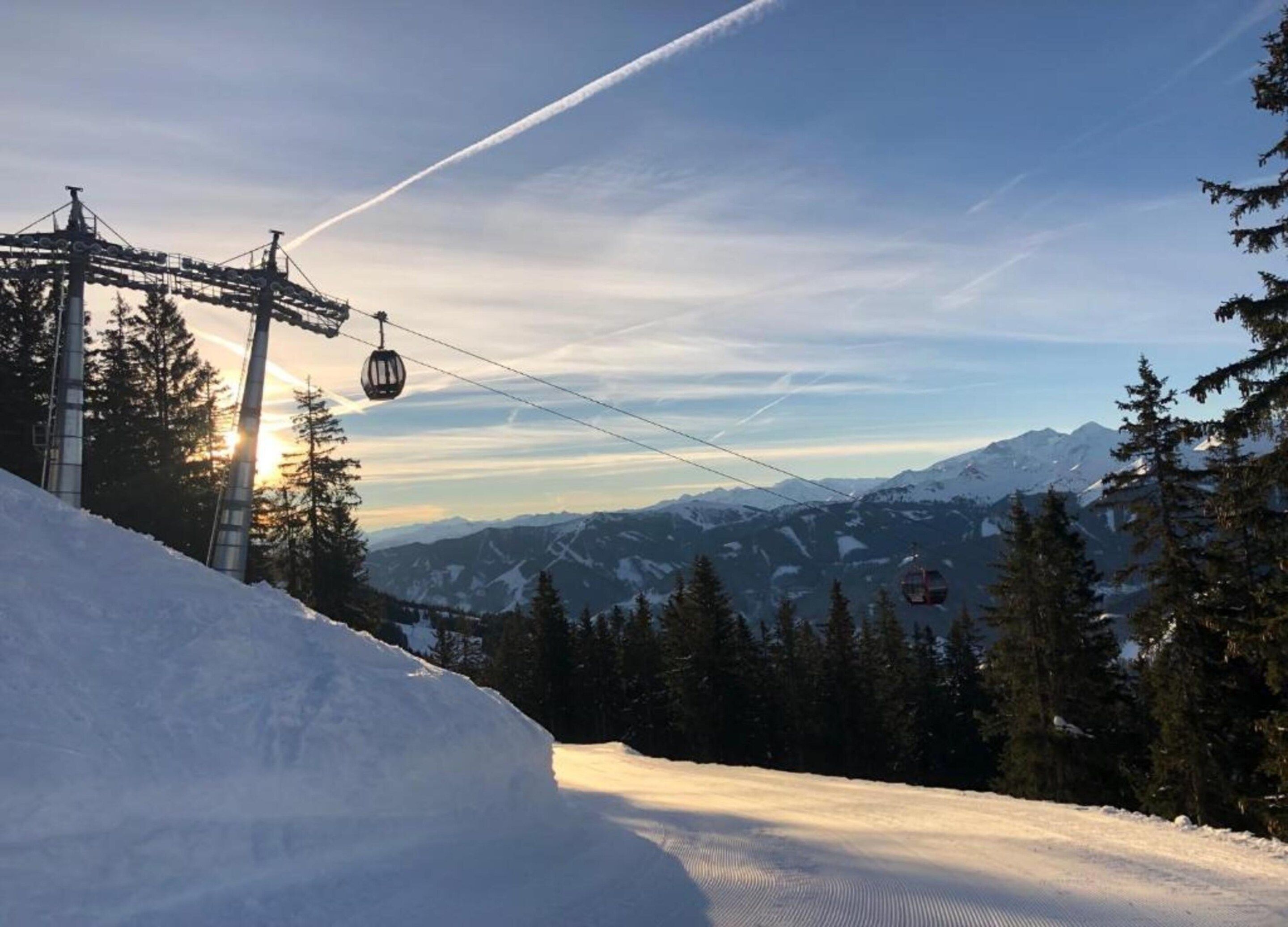 Een skigebied met kabelbaan, gondels en besneeuwde bergen op de achtergrond, onder een heldere lucht.
