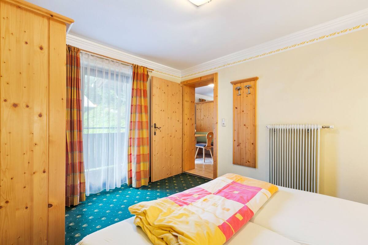 Una stanza con un letto, un armadio in legno, un termosifone e una porta che dà su un'altra stanza.