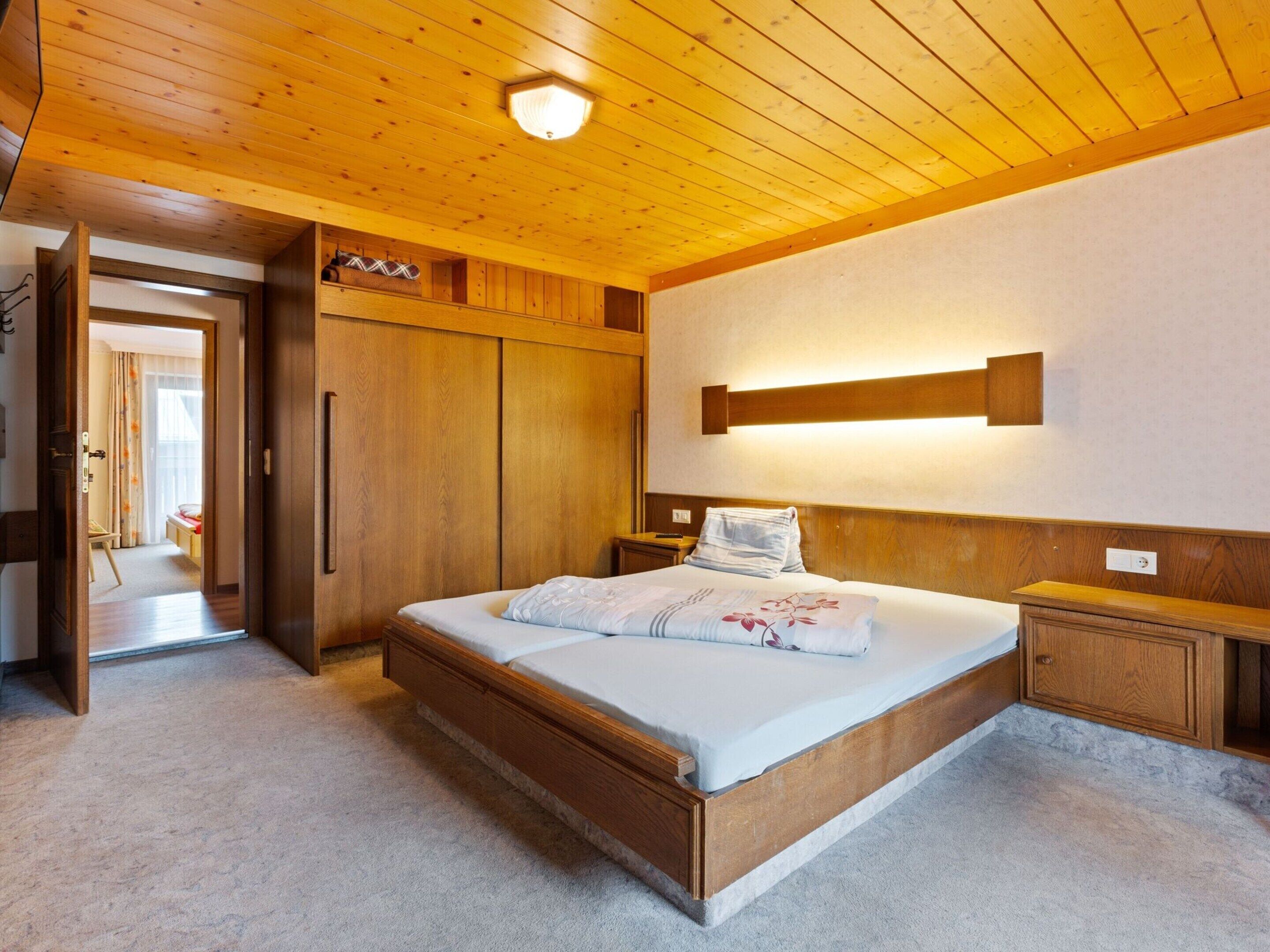Une chambre à coucher avec un lit en bois, une table de chevet, une armoire et un luminaire fixé au plafond.
