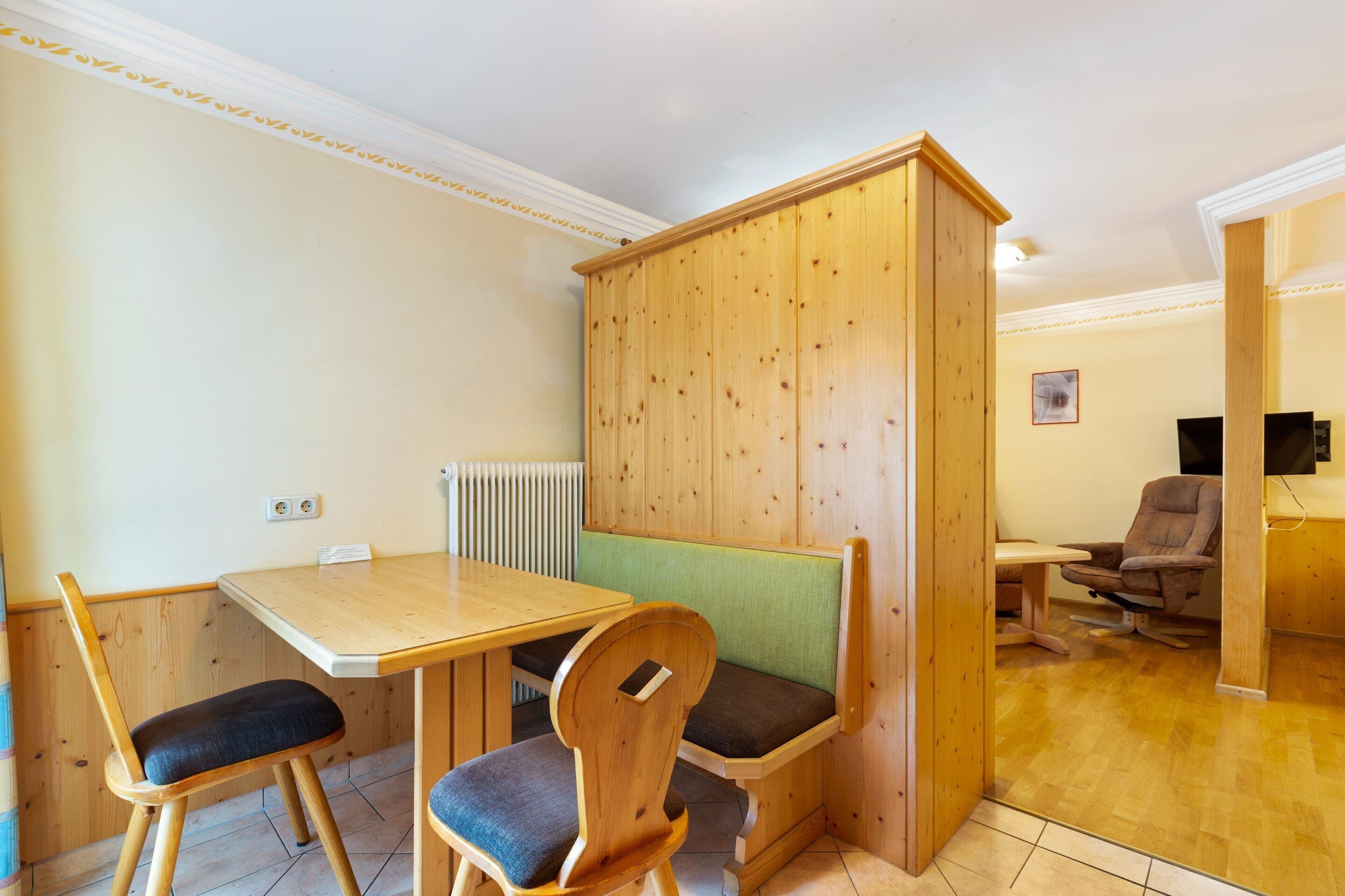 A small room with a wooden table and two chairs, a bench, and a wooden cabinet.