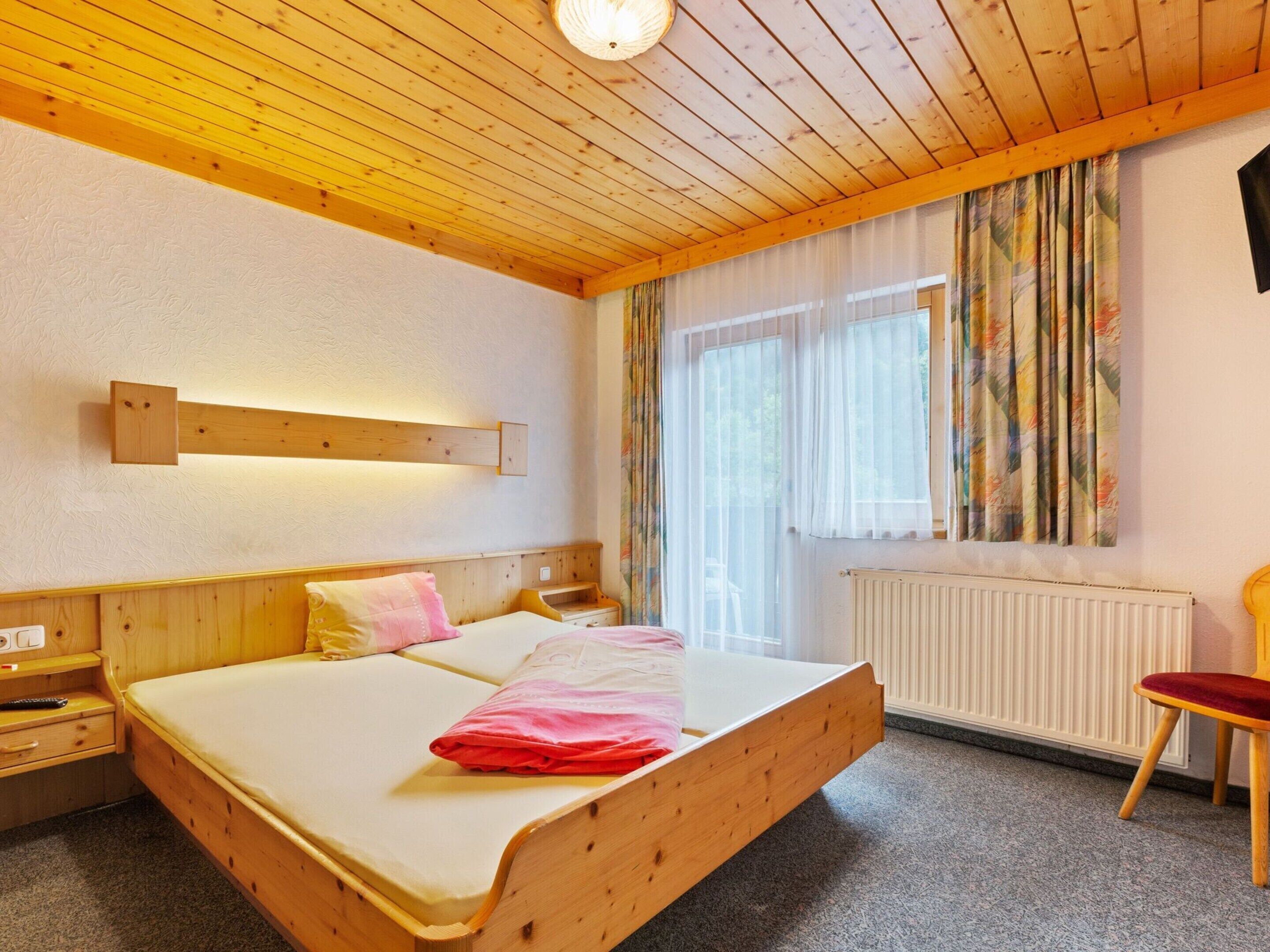 A wooden-framed bed with a white mattress, a bedside table, a chair, and a window with curtains.