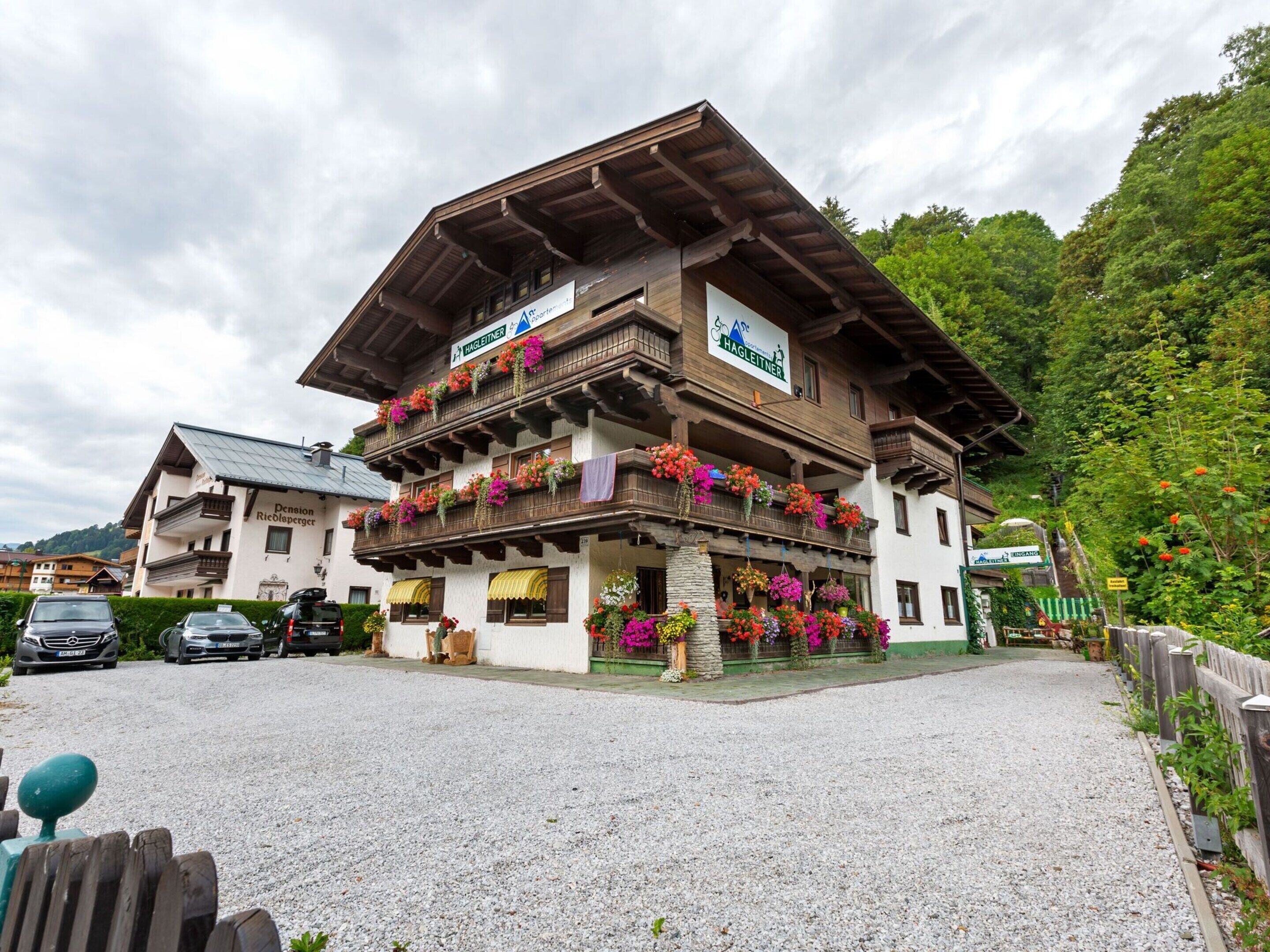Un bâtiment traditionnel en bois, doté de balcons ornés de fleurs colorées, une enseigne indiquant qu’il s’agit d’un restaurant, et une allée d’accès en gravier.