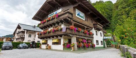 Un bâtiment traditionnel en bois, doté de balcons ornés de fleurs colorées, une enseigne indiquant qu’il s’agit d’un restaurant, et une allée d’accès en gravier.