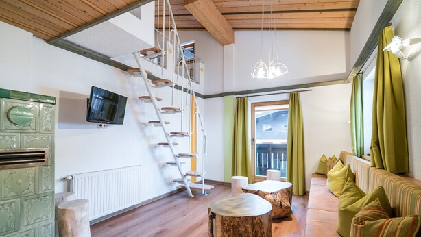 Un amplio salón con una escalera de madera, un sofá verde y un televisor fijado a la pared.