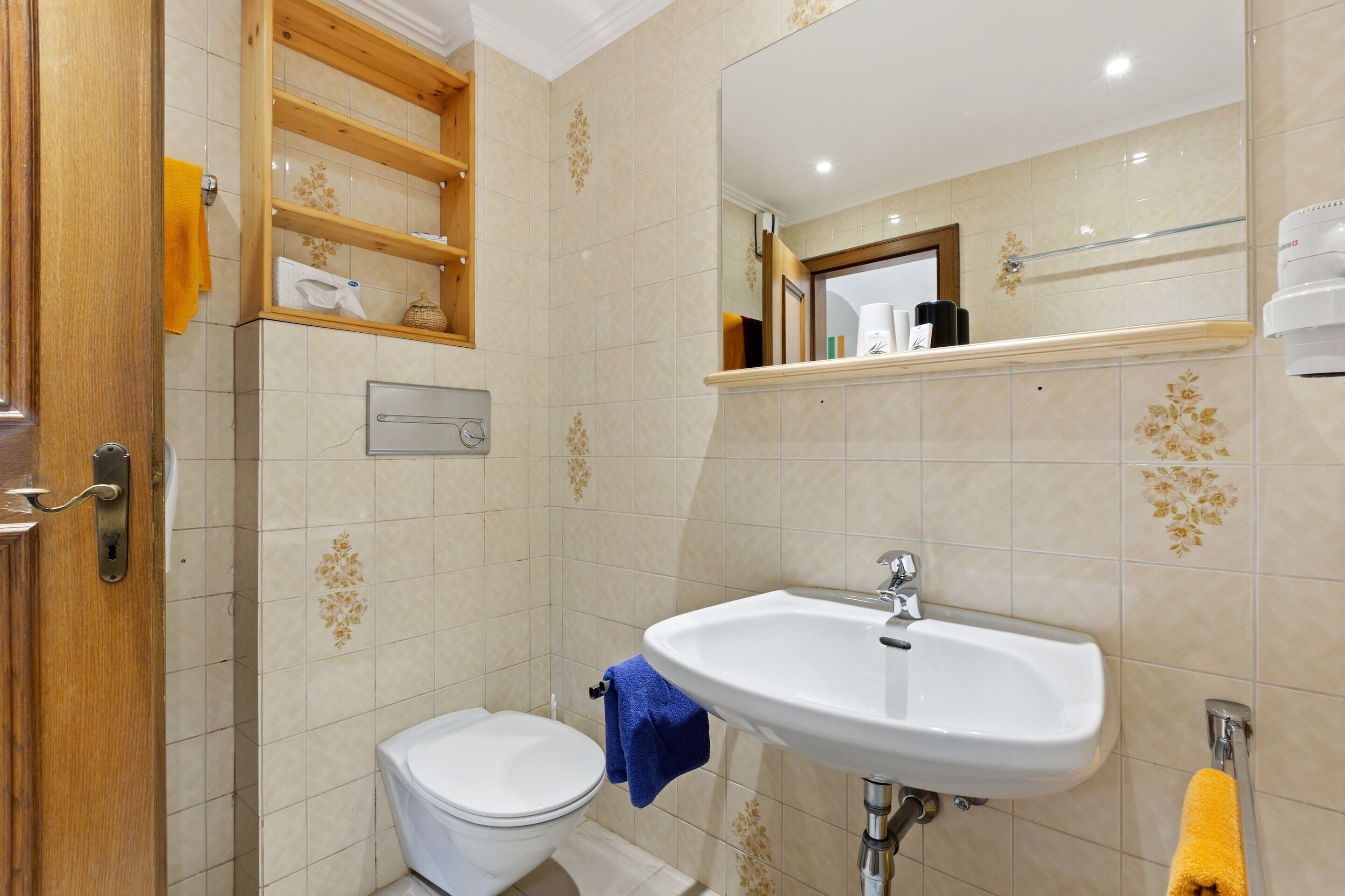 A bathroom with a toilet, sink, and wooden shelves above the toilet.
