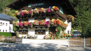 Un edificio de madera tradicional con balcones decorados con flores coloridas, un letrero que indica un restaurante y un coche estacionado frente a él.