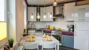 Een moderne keuken met witte kastjes, een eettafel met gele servetten en hangende lampen.