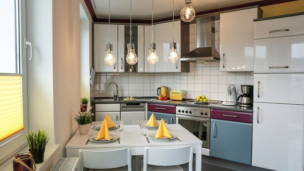 Una cocina moderna con armarios blancos, una mesa de comedor con servilletas amarillas y lámparas colgantes.
