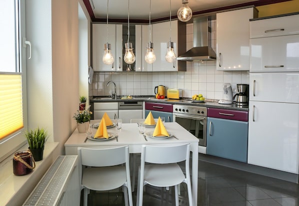 A modern kitchen with white cabinets, a dining table set with yellow napkins, and hanging light fixtures.