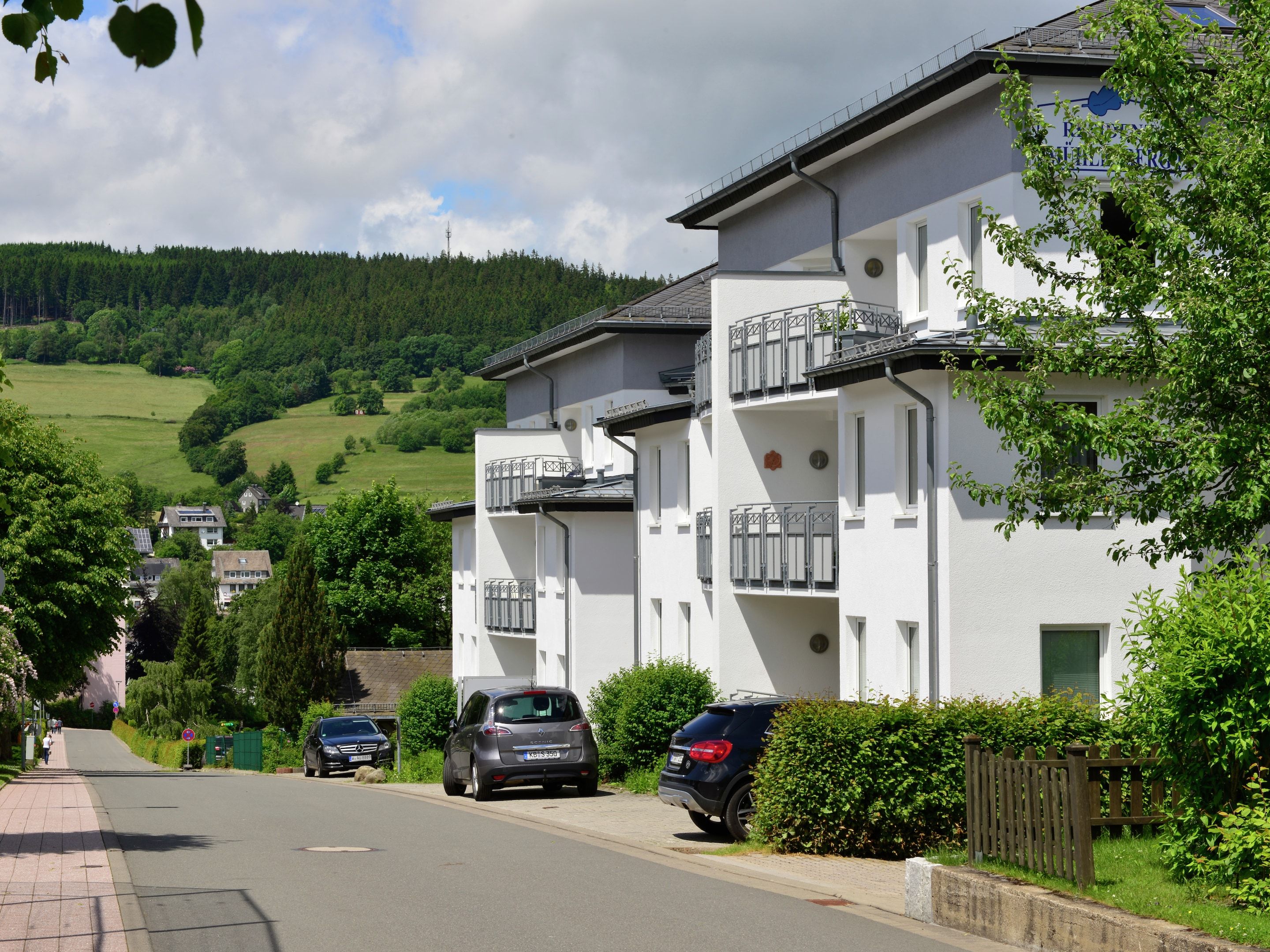 Un immeuble résidentiel doté de balcons, une rue pavée et un paysage vallonné en arrière-plan.