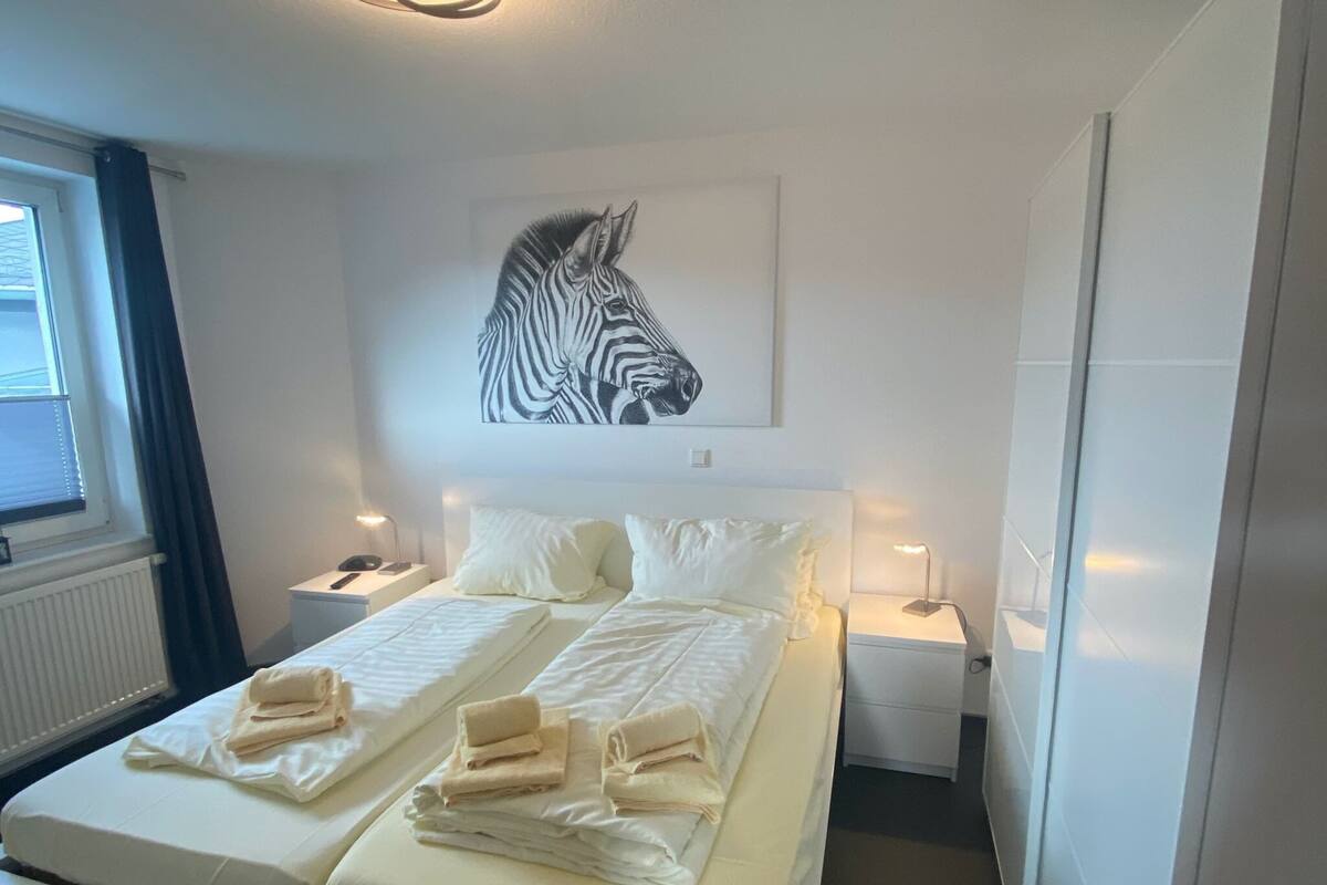 A hotel room with a bed, two bedside tables, a zebra artwork on the wall, and a window with curtains.