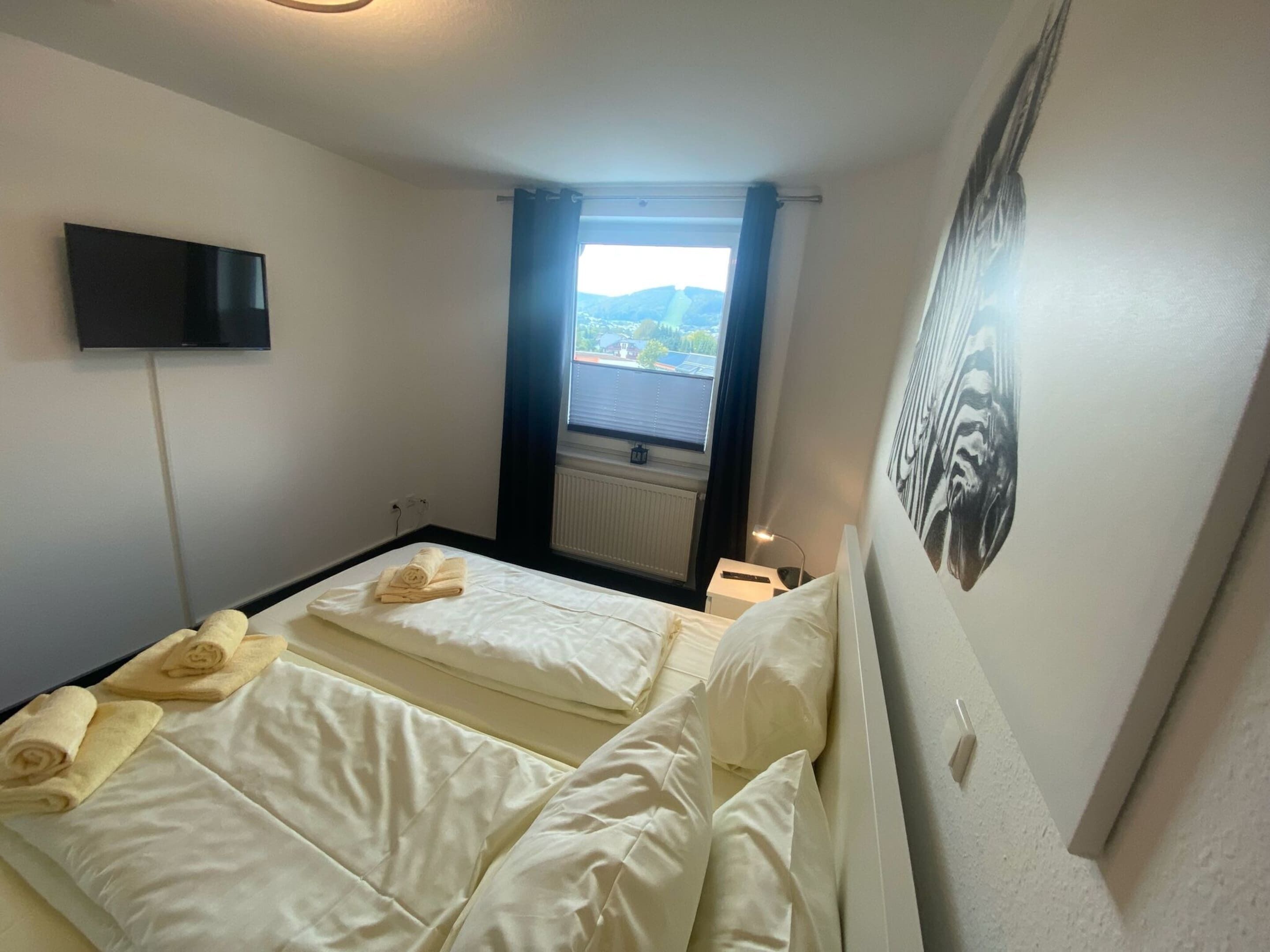 A hotel room with two beds, a flat-screen TV, a window with a view, and a painting on the wall.