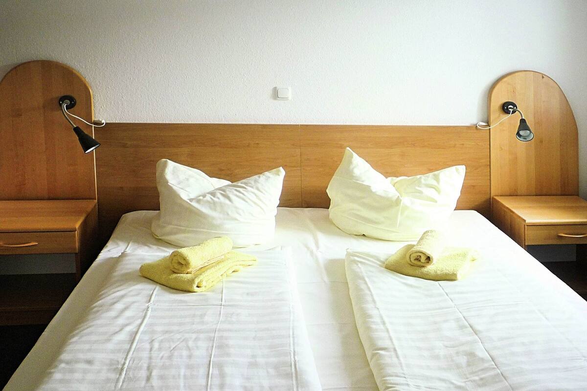 A neatly made bed with white linens, two pillows, and two rolled towels.
