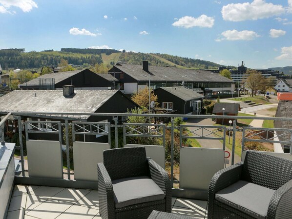 Una terraza con mobiliario de mimbre y vistas a un pueblo con casas y una colina al fondo.
