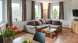 Een woonkamer met een bank, een salontafel, een televisie en een eettafel met fruit erop.
