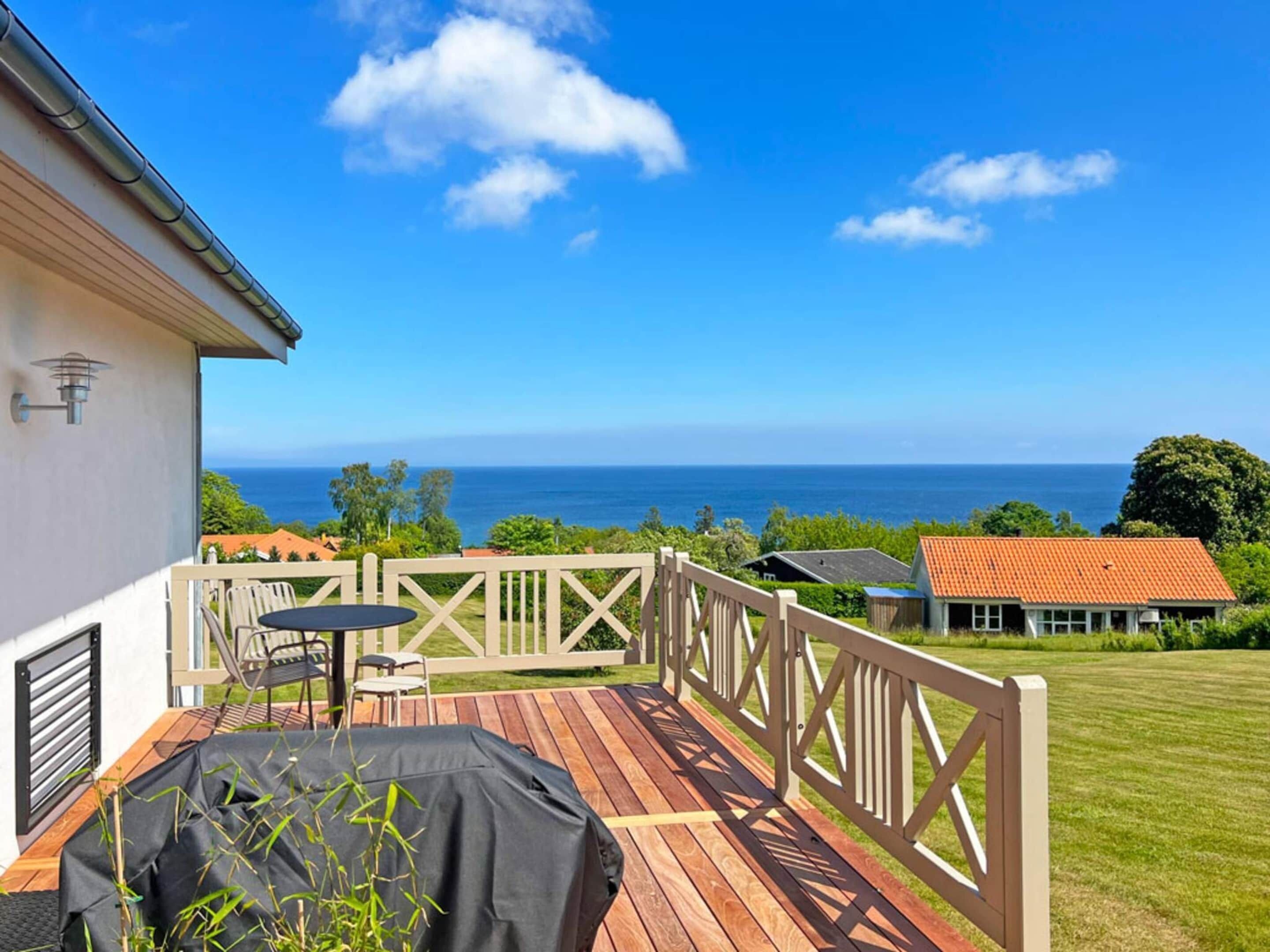 Eine Holzterrasse mit Tisch und Stühlen, mit Blick auf das Meer.