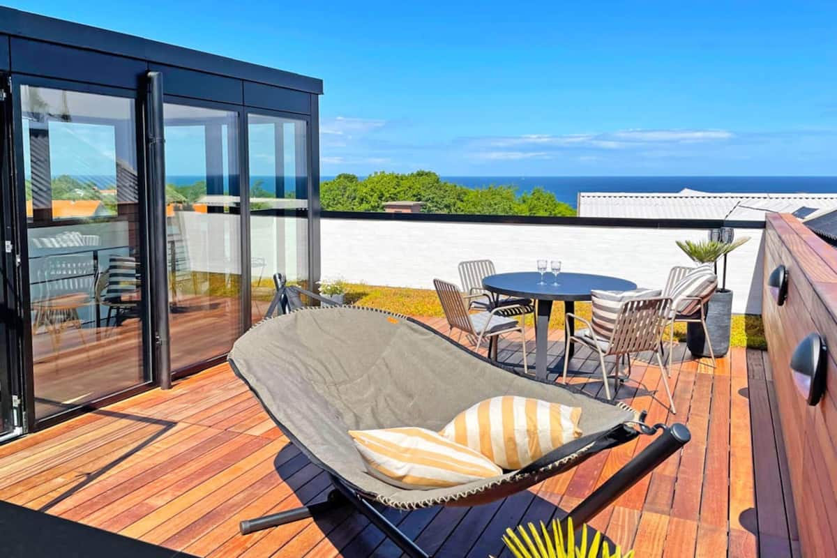 A deck with a lounge chair, a table, and chairs, overlooking a scenic view.