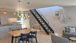 A modern kitchen with pendant lighting, a dining area with a wooden table and chairs, a staircase, and a living area with a sofa and cushions. - 4 Person Holiday Home in Allinge (Allinge)
