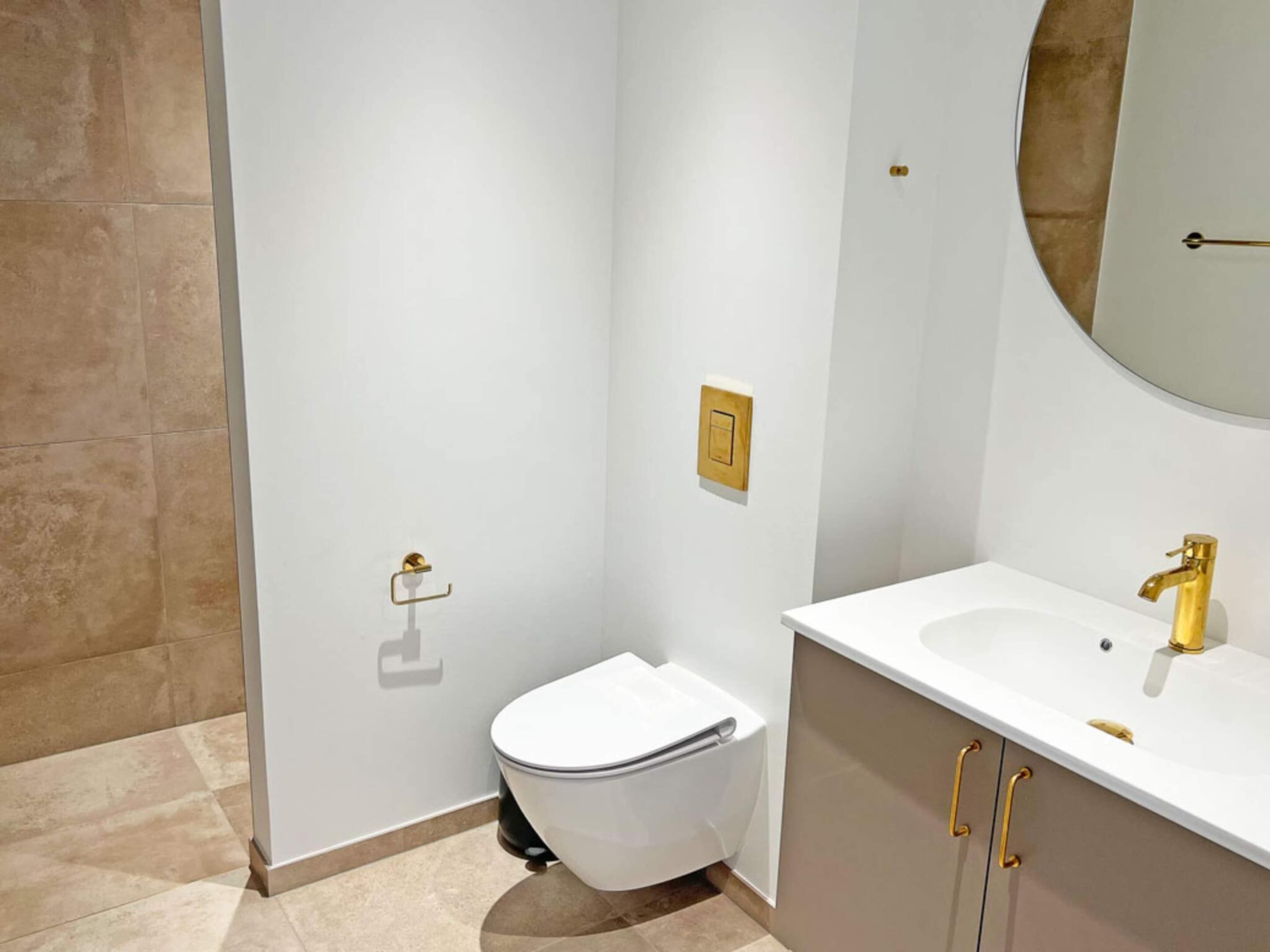 A modern bathroom with a white toilet, a vanity with a gold faucet, and a wall-mounted mirror.